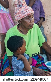 African Granny And Kid In The Village. Siting By The Wall In The Yard.