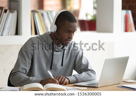 African guy e-learning sit at desk in public library, american student in headphones look at pc screen writing listened information preparing for university session or institute entrance exams concept