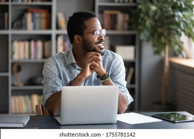 African guy freelancer or office worker take break from work seated at desk in front of laptop looking at window feels satisfied by accomplished work, visualizing relieving fatigue daydreaming concept - Powered by Shutterstock