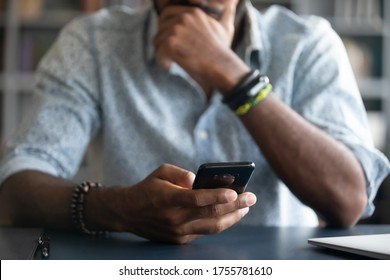 African guy holds cell phone close up view hands and device man feels concerned on background, received unpleasant sms, wait or missed important call, waste time online, addicted with internet concept