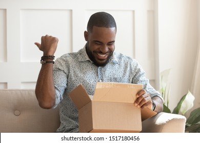 African Guy Holds On Lap Carton Box Looks Inside Feels Excited, Man Open Unpack Long-awaited Parcel, Satisfied Online Store Client, Trusted Transport Company, Fragile Goods Delivered Unscathed Concept