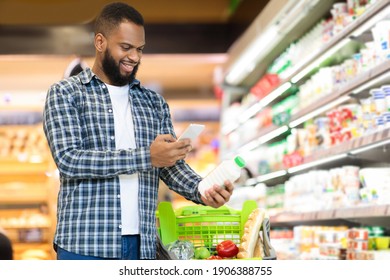 African Guy Scanning Product Via Phone Doing Grocery Shopping In Supermarket Store. Coupon Apps For Groceries. Customer Using Smartphone Application In Food Shop. Copy Space