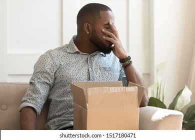 African guy sit on couch feels stressed saw that goods in package is damaged, man closed eyes cover face with hand received wrong items in parcel, dissatisfied client, complaints and refunding concept
