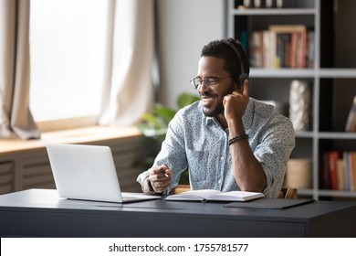 African guy student learn on-line use headphones with mic and pc holds pen takes notes in notebook sit at desk at home. Businessman wear headset talk by conference call do video chat working at office - Shutterstock ID 1755781577