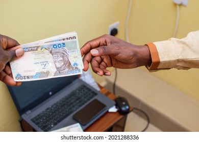 An african hand receiving Nigerian Naira notes, cash or currency with a laptop in the background