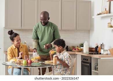 African Happy Father Cooking Breakfast For His Family While They Eating At The Table In The Kitchen