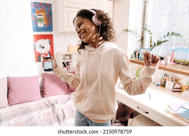 African Happy Teen In Headphones Listening To Music And Dancing In Her Cozy Room At Home