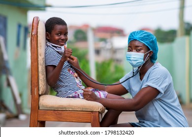 African Health Professional Or Physician Wearing Face Mask,auscultating Chest Of A Child Wearing Homemade Mask Under Chin,giving A Thumbs Up In Covid-19 Pandemic