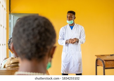 African High School Teacher Wearing A Lab Coat And Face Mask In Class Talking To The Class Pupils