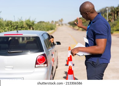 african instructor teaching learner driver to park a car in testing ground