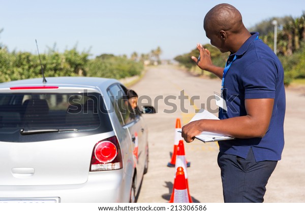 african instructor teaching learner driver to park\
a car in testing ground