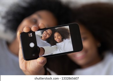 African kid lying with mother take make selfie on phone, showing photo to camera, close up hand and device. New generation, gadgets easy usage in everyday life, sisters entertaining having fun concept