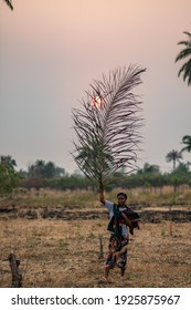 African Lady Holding A Palm Frond High Up With The Sun Setting Behind It