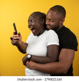 An African Lady Looks Suprised As She Looks Into Her Phone With Her Man