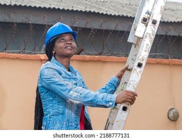 African lady or woman from Nigeria with blue safety helmet, climbing a ladder and looking up as she represents industrial professionals like construction specialist, builders, architect and engineer - Powered by Shutterstock