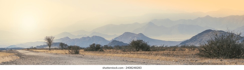 African landscape at sunrise with morning haze and silhouettes of mountains in Damaraland valley, Namibia. Wildlife travelling, adventures and safari tours on roads to Africa, wide panoramic view. - Powered by Shutterstock