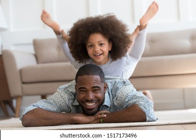 African little daughter perform yoga boat pose on father back, family lie on carpet on warm floor kid girl do spine muscle strengthening exercise, sporty lifestyle, have fun at home with child concept - Powered by Shutterstock