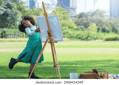 African little girl picnicking at the park enjoying painting on canvas on a painting easel, amidst the bright summer atmosphere - Powered by Shutterstock