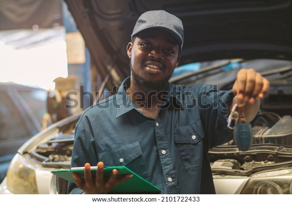 African maintenance male\
checking car and hands the customer the car keys after the car\
repair is complete