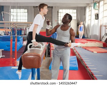 African male coach helping teenage boy doing gymnastic exercises on equipment - Powered by Shutterstock