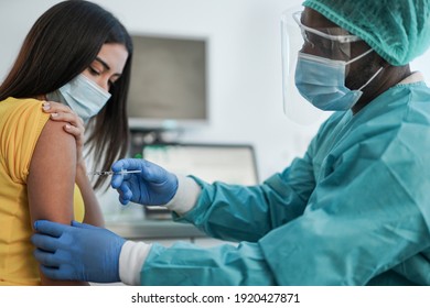 African male doctor with syringe injecting vaccine on young woman patient against coronavirus - Medical worker inside hospital wearing surgical mask and hazmat suit