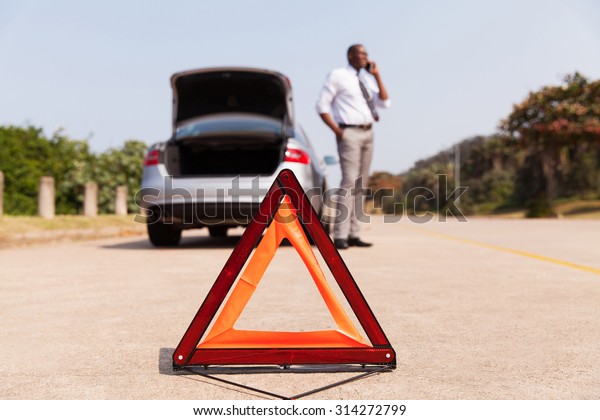 african male driver calling for help after car\
broke-down by the side of the\
road