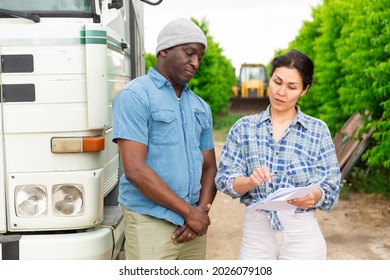 African Male Farmer And Asian Woman Discussing Some Papers, Standing Near Car At Orchard