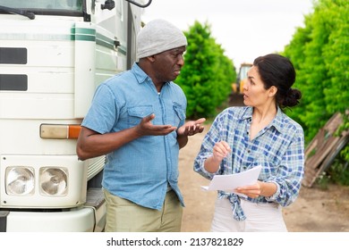 African Male Farmer And Asian Woman Discussing Some Papers, Standing Near Car At Orchard