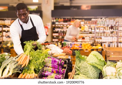 African Male Grocery Worker In Apron Arranging Fresh Vegetables On Shop Counter