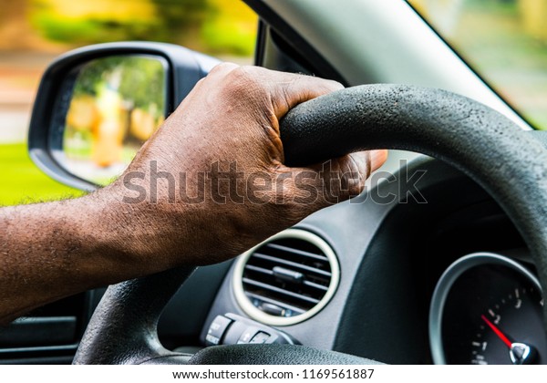 African Male hands on the steering wheel of a car\
while driving.Driver holding steering wheel. Black Man hands\
holding a steering wheel confidently. Hands on wheel - Man driving\
car - Africa