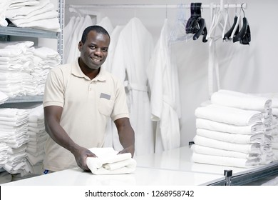  African Male Hotel Worker Folds A Clean White Towel. Hotel Staff Workers. Hotel Linen Cleaning Services.