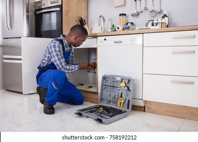 African Male Plumber Fixing Sink Pipe In Kitchen