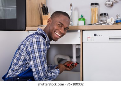 African Male Plumber Fixing Sink Pipe In Kitchen