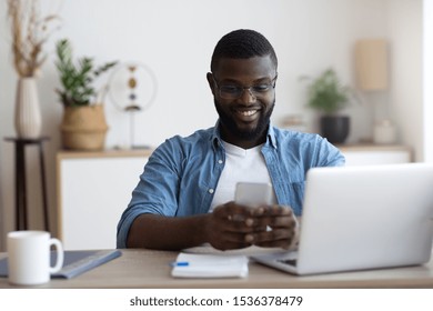 African male worker using both phone and computer in workplace.