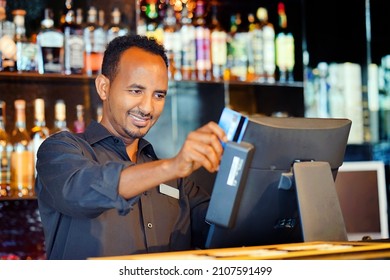 African Man Bartender In Hotel Bar. African Male Bartender At The Cash Register