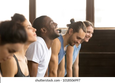 African Man Beginner Laughing Having Fun Trying To Do Yoga Pose, Push Ups Plank Or Stretching In Upward Facing Dog Exercise At Group Training Class With Multiracial Diverse People, Closeup Side View