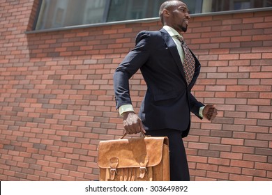 The African Man As Black Businessman With A Briefcase Running In A City Street On A Background Of Red Brick Wall