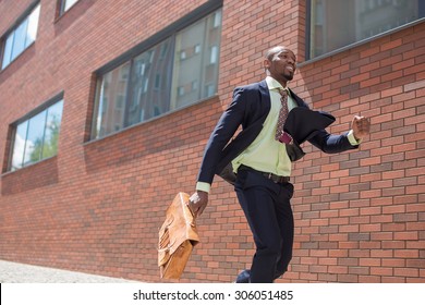 The African Man As Black Businessman With A Briefcase Running In A City Street On A Background Of Red Brick Wall