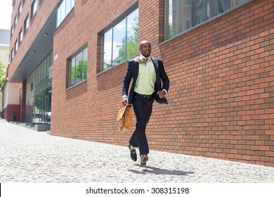 The African Man As Black Businessman With A Briefcase Running In A City Street On A Background Of Red Brick Wall