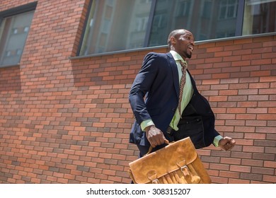 The African Man As Black Businessman With A Briefcase Running In A City Street On A Background Of Red Brick Wall