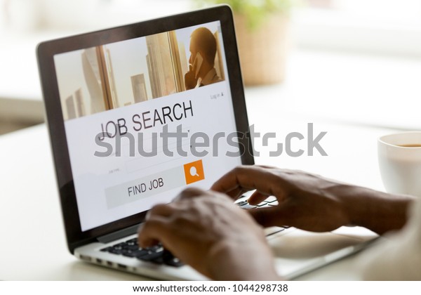 African man browsing work opportunities online using\
job search computer app, black jobless seeker looking for new\
vacancies on website page at laptop screen, recruitment concept,\
rear close up view