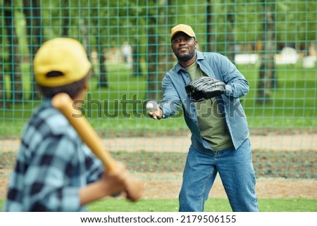 African man catching ball with glove throwing by his son during baseball game outdoors