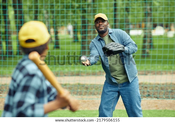 African man catching ball with glove\
throwing by his son during baseball game\
outdoors