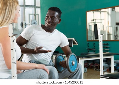 African man and Caucasian woman standing and talking  near simulators at gym  - Shutterstock ID 1345203011