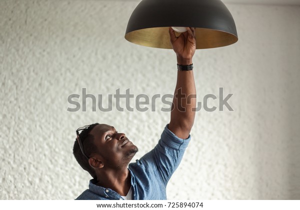 African man changing light bulb in coffee shop\
, installing a fluorescent light\
bulb