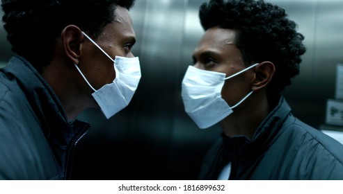 African Man Checking Cellphone Wearing Covid-19 Mask Inside Elevator Looking At Mirror Reflection