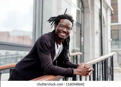 African Man With Dreadlocks And Glasses Standing On The Street With A Big Smile Leaning On The Railing