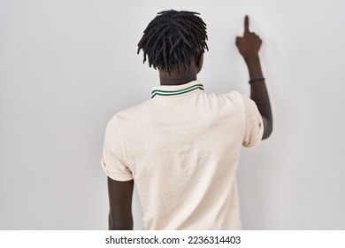 African man with dreadlocks standing over isolated background posing backwards pointing ahead with finger hand 