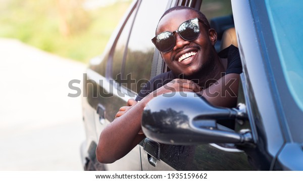 African man driver wearing sunglasses and\
smiling while sitting in a car.16:9\
style