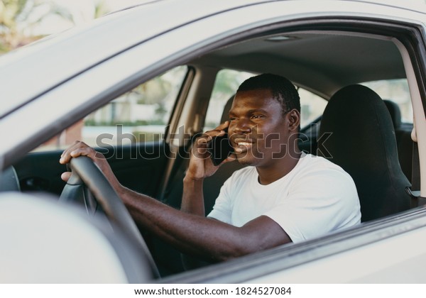 African man driving a car smiling and talking on\
the phone